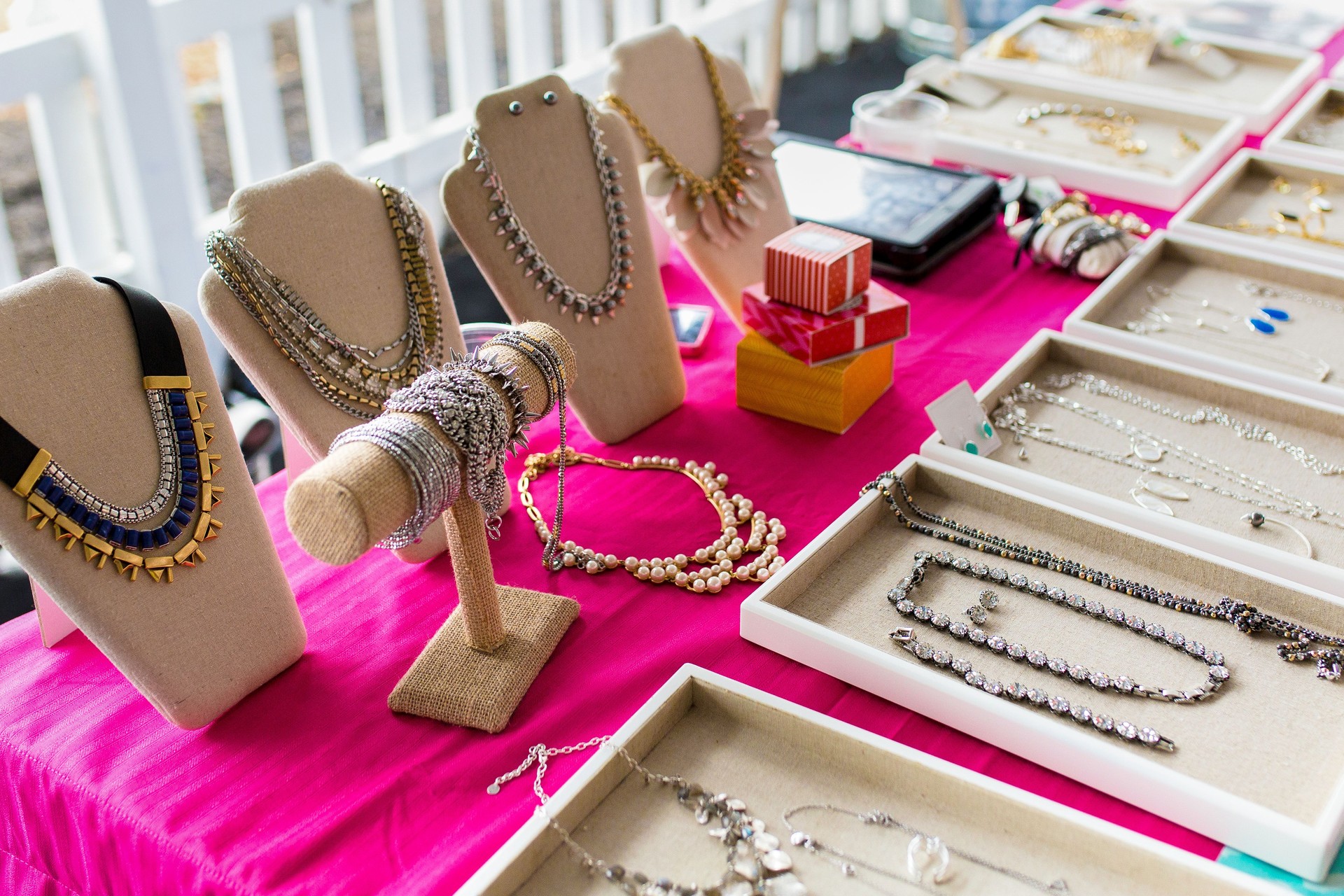 Display Of Various Jewelry Items On Stands With A Bright Pink Cloth Background.